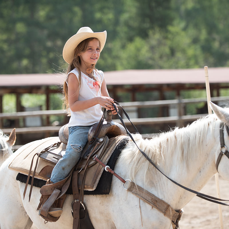 Little cowgirl comfortably sitting on white horse
